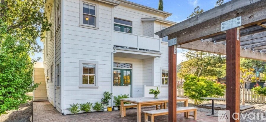 A white two-story house with a balcony and a wooden pergola.