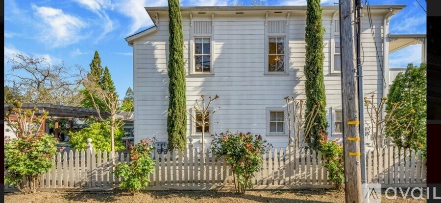 A white house with a fence and green plants in front.