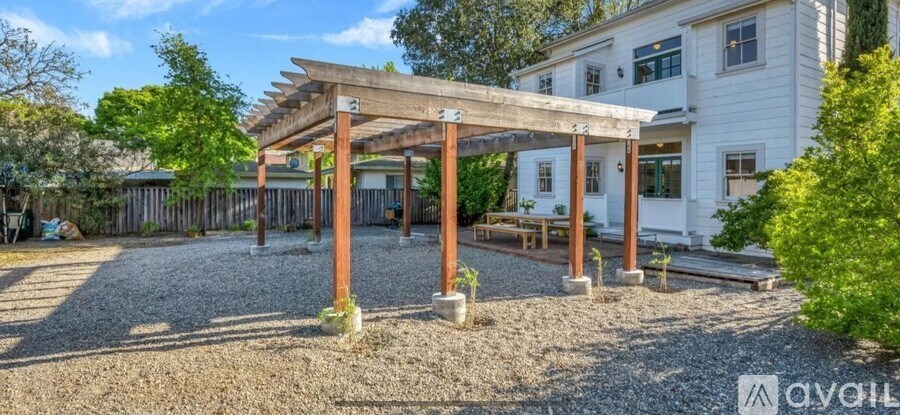 A white house with a wooden pergola over a gravel area.