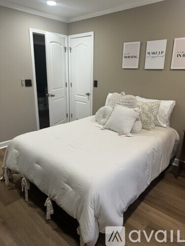 A bedroom with a white bed and pillows, a white door, and a wall with three framed pictures.