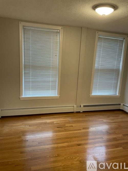 A room with wooden floors and two windows with blinds.