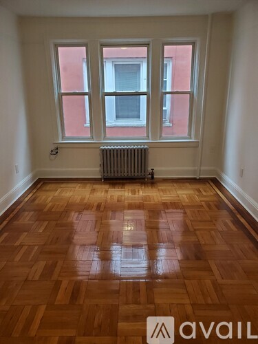 A room with wooden flooring and a window with a view of a building.