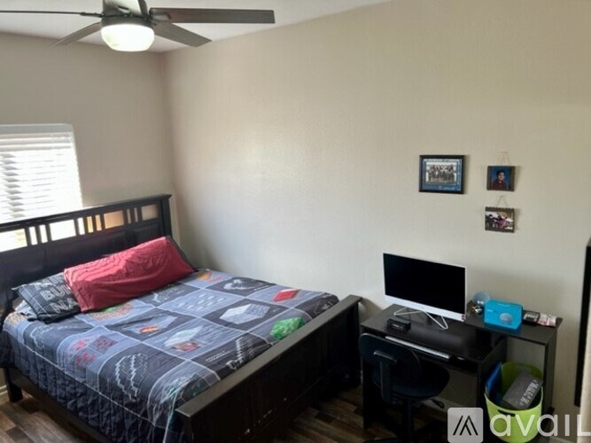 A bedroom with a bed, desk, and ceiling fan.