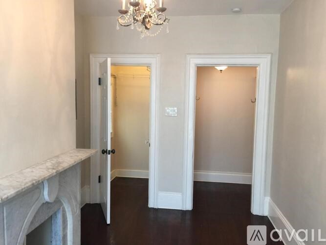A chandelier hangs over a white fireplace in a room with two doors.