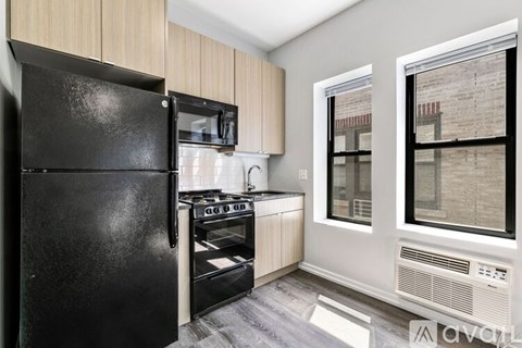 A black refrigerator is in a kitchen with a window.