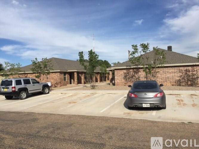 A parking lot with a grey car and a silver SUV in front of a building with a brick wall.