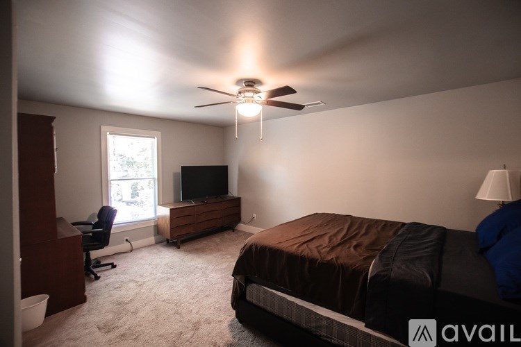 A bedroom with a bed, a chair, a television, and a ceiling fan.