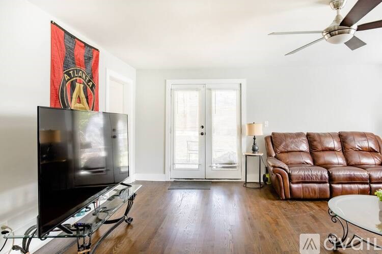 A living room with a television, leather couch, and a ceiling fan.