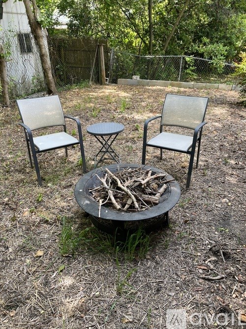 A fire pit with a metal grate and two chairs are in a backyard.