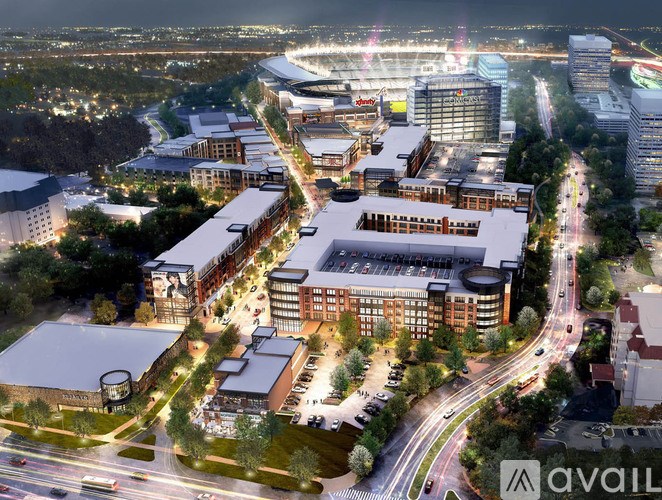 A cityscape at night with a large building complex in the foreground and a stadium in the background.