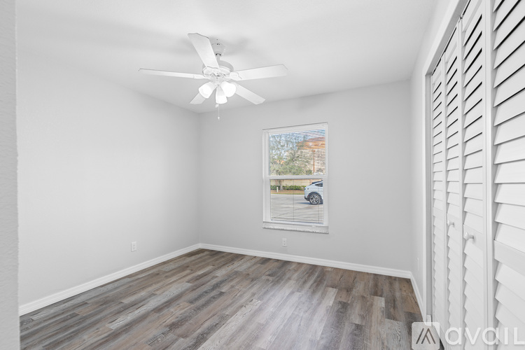 A room with a ceiling fan and a window showing a car and trees outside.