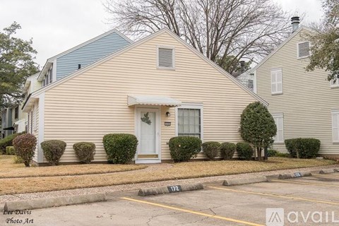 A house with a white door and windows is surrounded by bushes.
