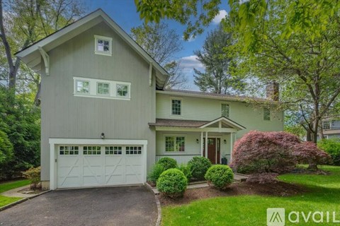 A house with a white exterior and a brown roof is surrounded by greenery.