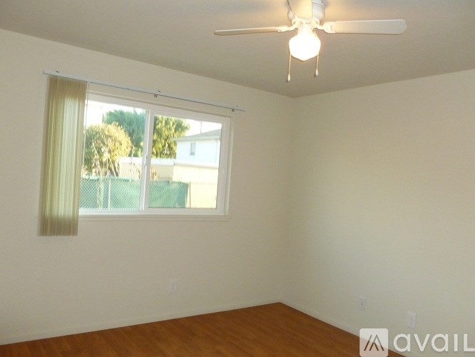 A room with a ceiling fan and a window with a view of a fence and trees.