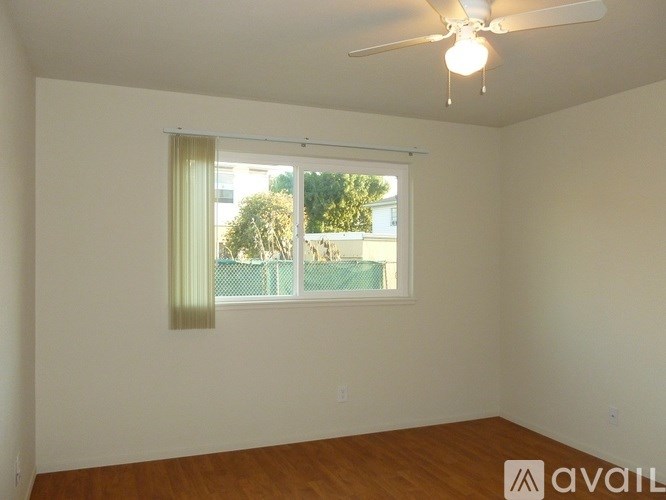 A room with a ceiling fan and a window with a view of a pool and trees.