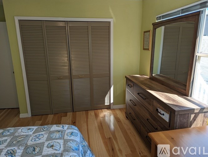 A bedroom with a bed, wooden dresser, and window with blinds.