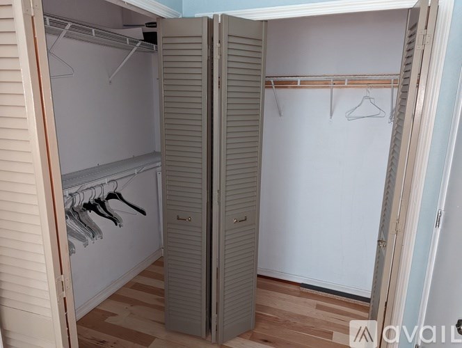 A white closet with clothes hanging on hangers.