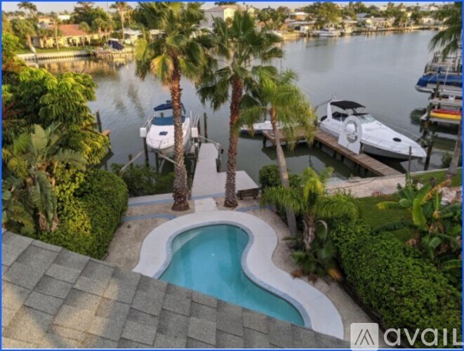 A swimming pool is surrounded by palm trees and a dock with boats.