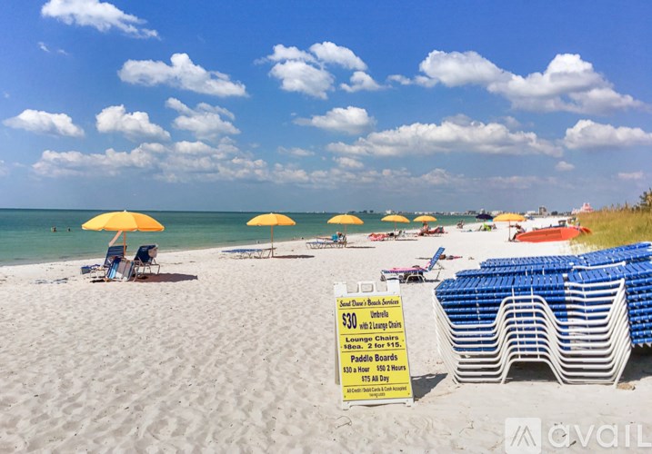 A beach scene with a sign offering lounge chairs and paddle boards for rent.