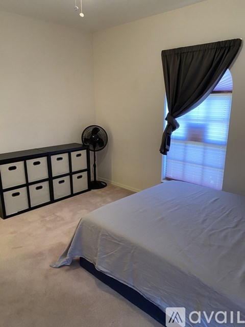 A bedroom with a bed, a fan, and a window with curtains.