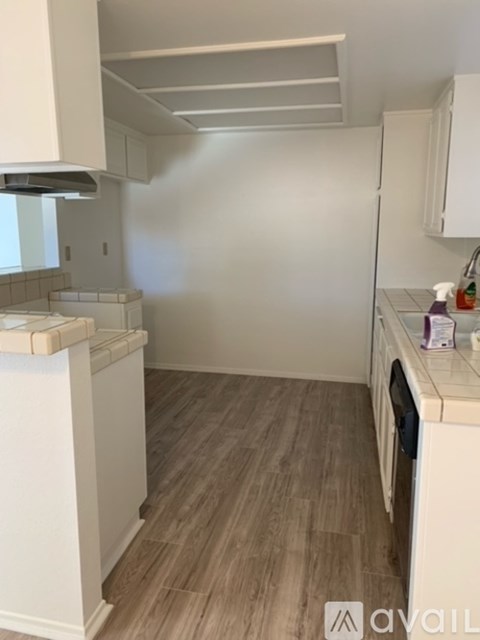 A small, clean kitchen with white cabinets and a wooden floor.