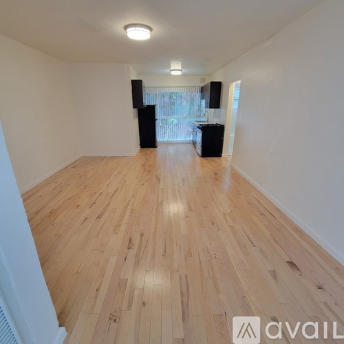 A room with wooden flooring and a kitchen area in the background.