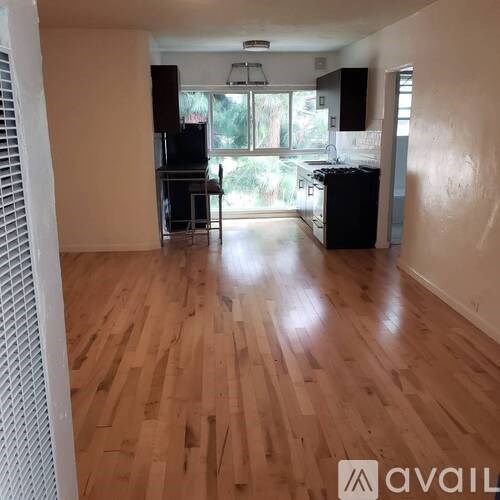 A room with wooden flooring and a kitchen area in the background.