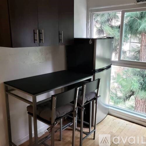 A black table and two chairs are in front of a window with a view of trees.