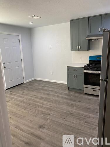A kitchen area with a white door, grey cabinets, and a wooden floor.