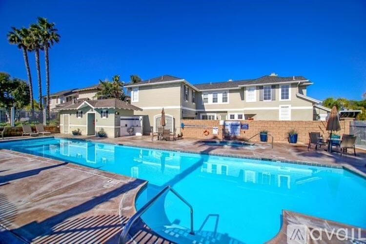 A swimming pool in front of a house with a fence and palm trees.