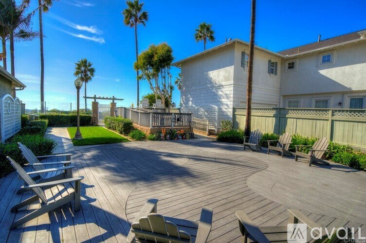 A wooden deck with chairs and a table is surrounded by a fence and palm trees.