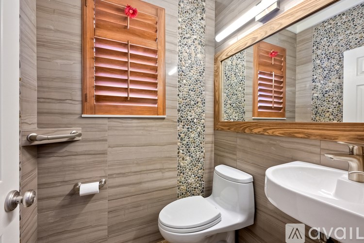 A bathroom with a toilet, sink, and wooden window blinds.