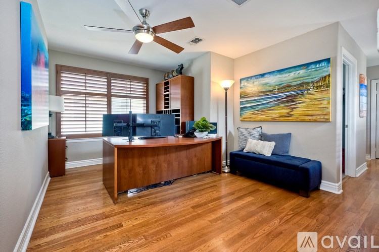 A room with a wooden desk and a blue couch with a painting on the wall.