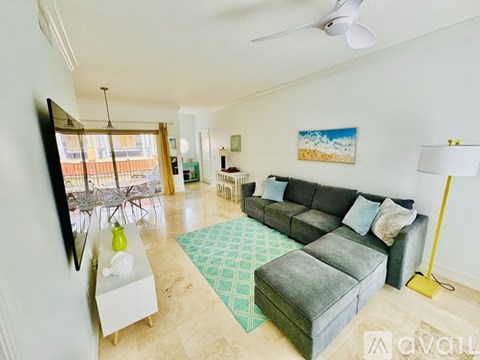 A living room with a grey couch, a green rug, and a painting of a beach scene on the wall.