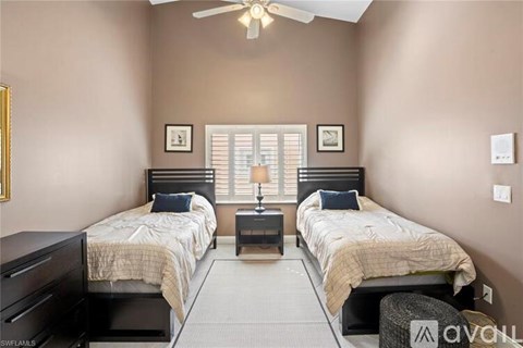 A bedroom with two beds, a ceiling fan, and a window with blinds.