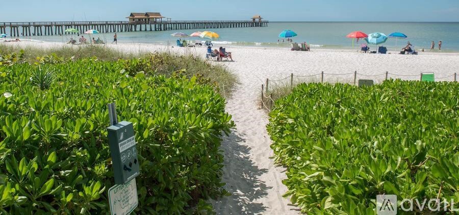 A beach scene with a pier in the distance and people on the beach.