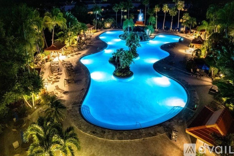 A large outdoor swimming pool surrounded by palm trees at night.