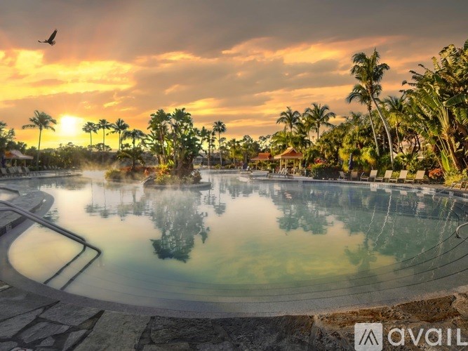 A beautiful sunset view of a pool surrounded by palm trees.