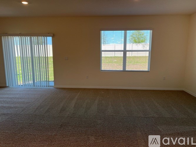 A room with a carpeted floor and a large window with a view of a fence and trees.