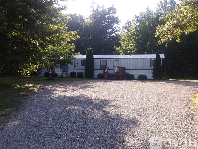 A gravel driveway leads to a white house surrounded by trees.