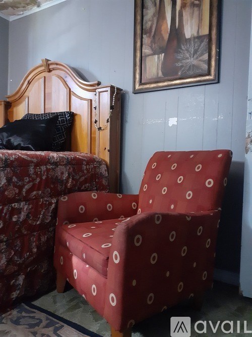 A red chair with white circles on it sits in front of a bed.