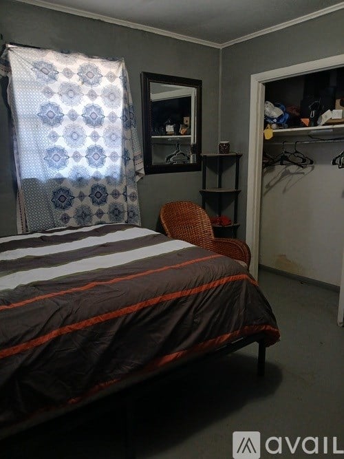 A bedroom with a bed, chair, and a window with a curtain.