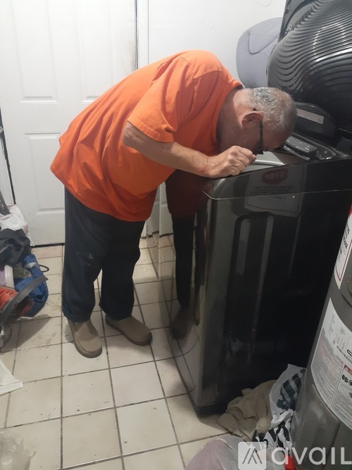 A man in an orange shirt is bending over a black appliance.