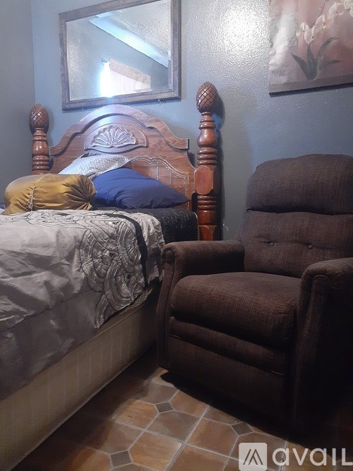 A brown recliner chair is in front of a bed with a white comforter and a blue pillow.