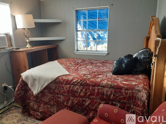 A bedroom with a red bedspread and a window with a blue curtain.