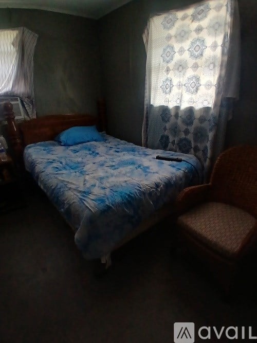 A bedroom with a bed, chair, and window with curtains.