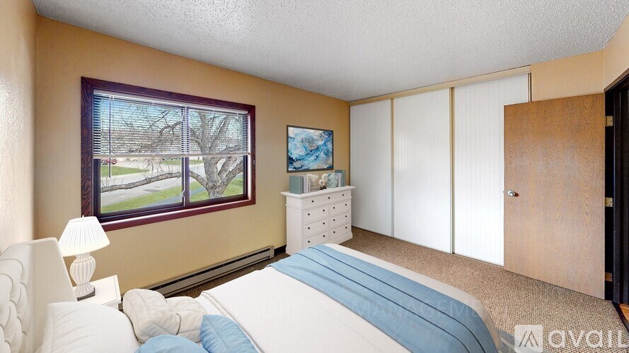 A bedroom with a large bed and a window overlooking a tree-lined street.