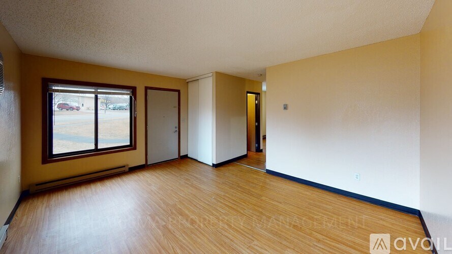 A room with wooden floors and a window with a view of a parking lot.
