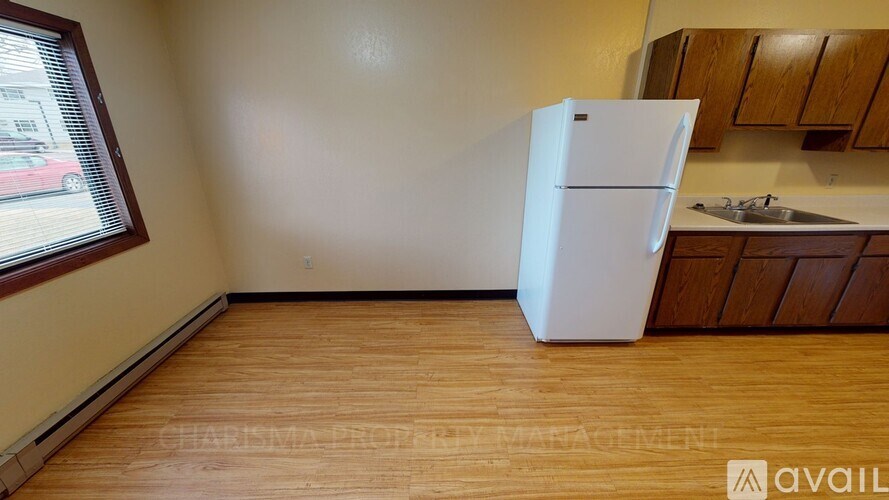 A white refrigerator is in a kitchen with wooden floors and cabinets.