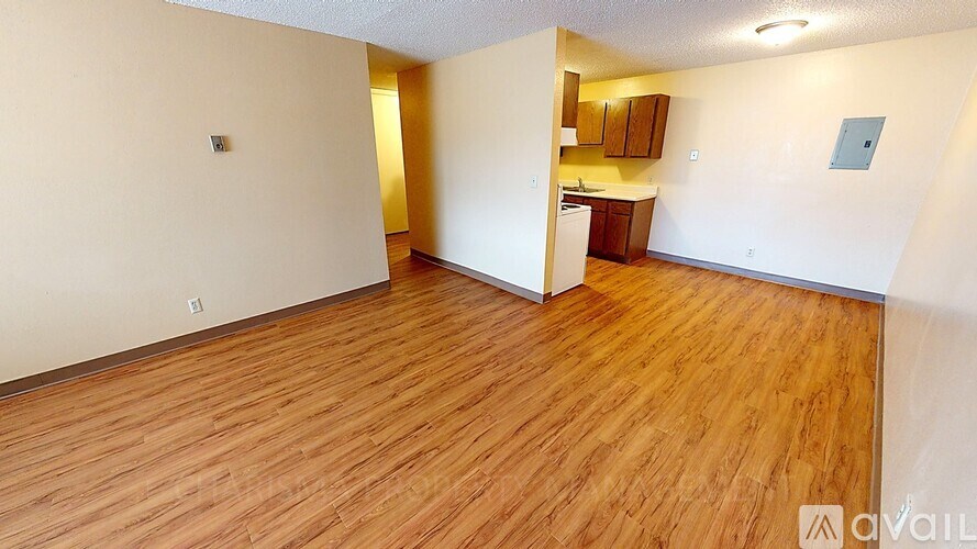 A room with wooden flooring and a kitchenette in the background.